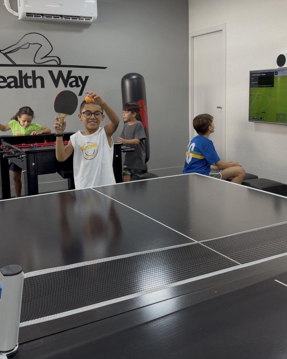 Crianças jogando pingue-pongue e pebolim no espaço kids da Health Way